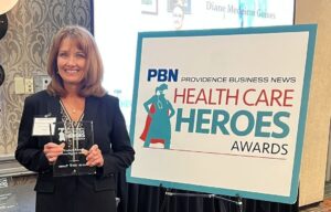 Smiling woman in a dark blazer holds a glass award at the Health Care Heroes Awards event.