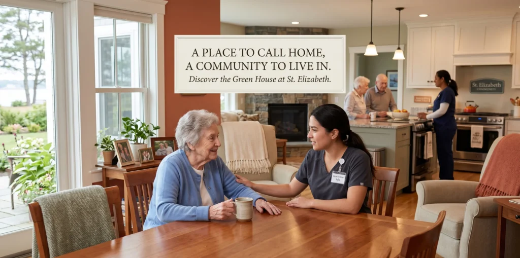A heartwarming scene inside a "Green House" small-home nursing facility at St. Elizabeth Community in Rhode Island. An elderly resident in a blue cardigan sits at a large wooden dining table, smiling while talking with a young caregiver in grey scrubs. In the open-concept background, other seniors and staff gather in a modern kitchen. Text overlay reads: "A PLACE TO CALL HOME, A COMMUNITY TO LIVE IN. Discover the Green House at St. Elizabeth."