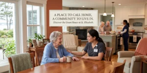 A heartwarming scene inside a "Green House" small-home nursing facility at St. Elizabeth Community in Rhode Island. An elderly resident in a blue cardigan sits at a large wooden dining table, smiling while talking with a young caregiver in grey scrubs. In the open-concept background, other seniors and staff gather in a modern kitchen. Text overlay reads: "A PLACE TO CALL HOME, A COMMUNITY TO LIVE IN. Discover the Green House at St. Elizabeth."