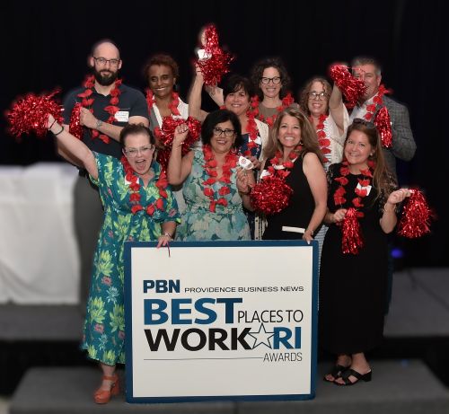 Group of award winners on stage posing with red pom-poms around a sign that reads 'PBN Best Places to Work Awards'.