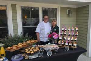 Culinary excellence at Saint Elizabeth Assisted Living East Greenwich - Saint Elizabeth Community Two vendors pose for a photo at a backyard dessert display with pastries and fruit-topped cream desserts on skewers outdoors.
